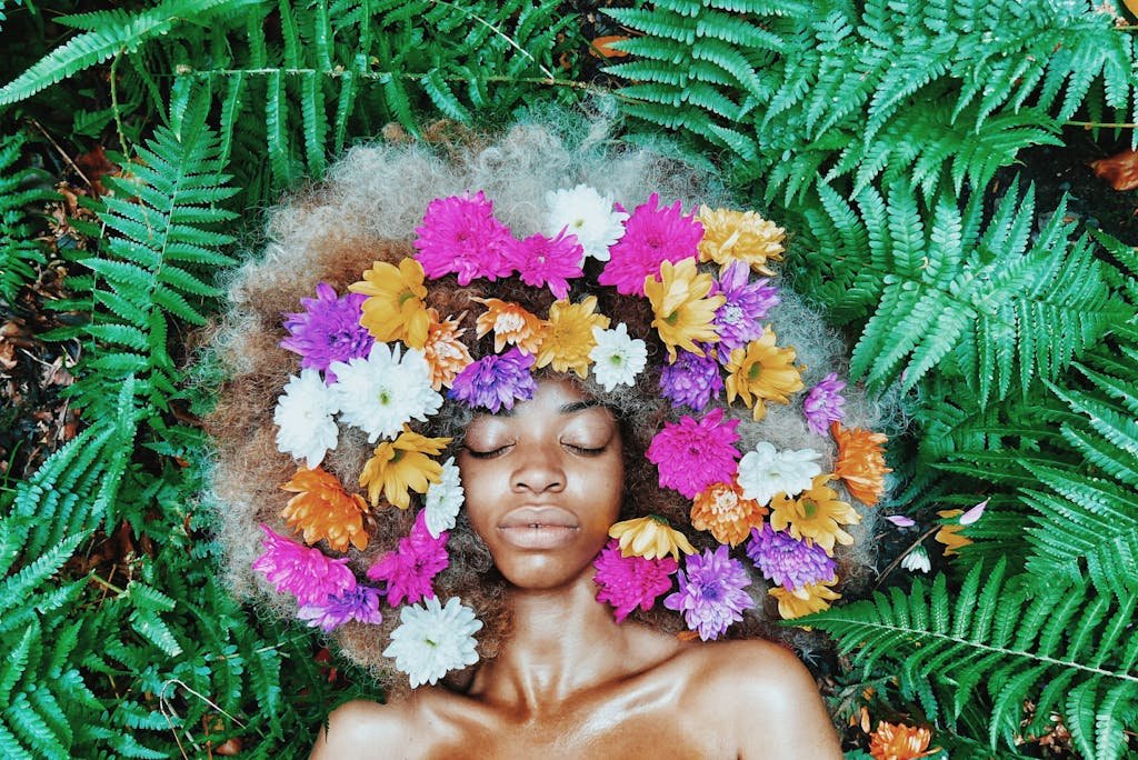 A serene portrait of a woman with flowers in her afro, surrounded by lush green ferns.
